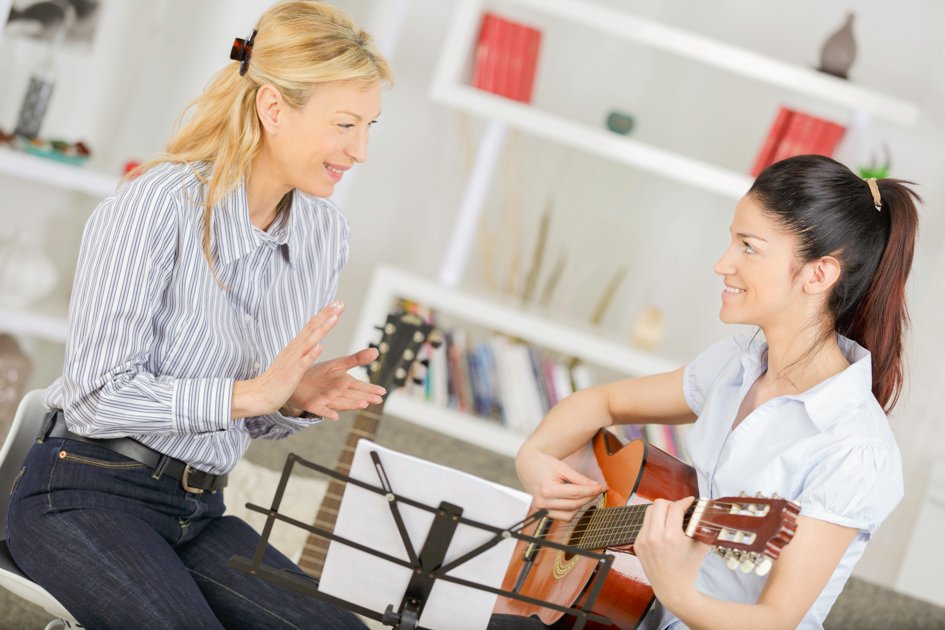 lady teaching young woman how to play guitar